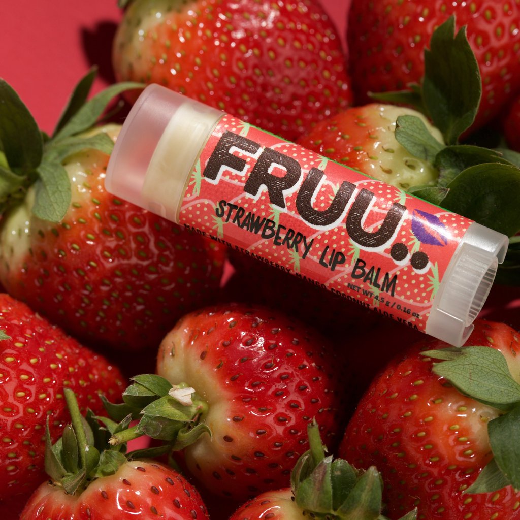 A strawberry lip balm by FRUU shown on top of a bed of strawberries