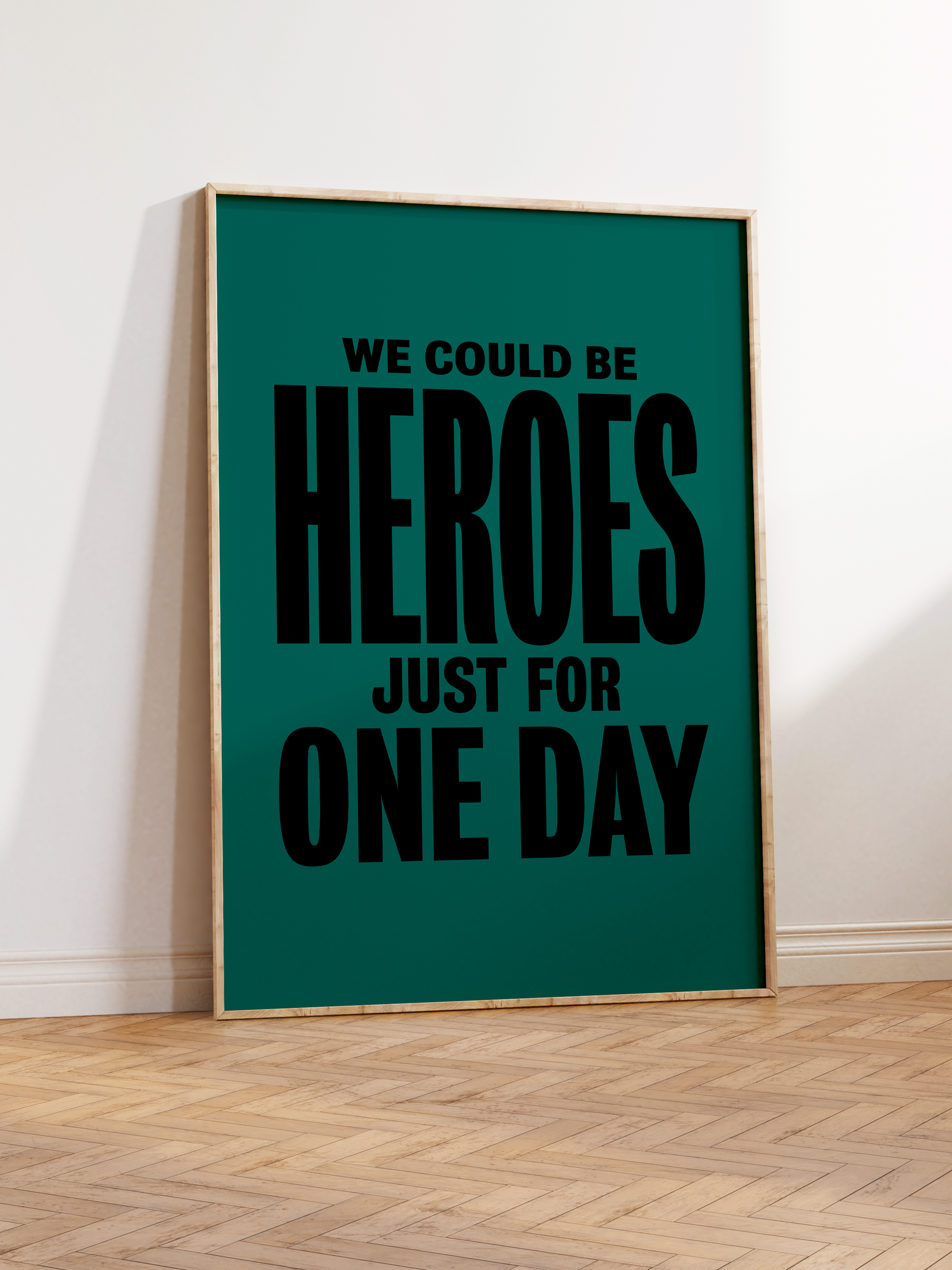 An image of an art print in a frame featuring the lyrics to the David Bowie song Heroes 'We could be heroes just for one day' in black block capitals on a teal background.