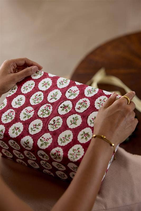 Person wrapping a gift with red floral paper on a wooden table.