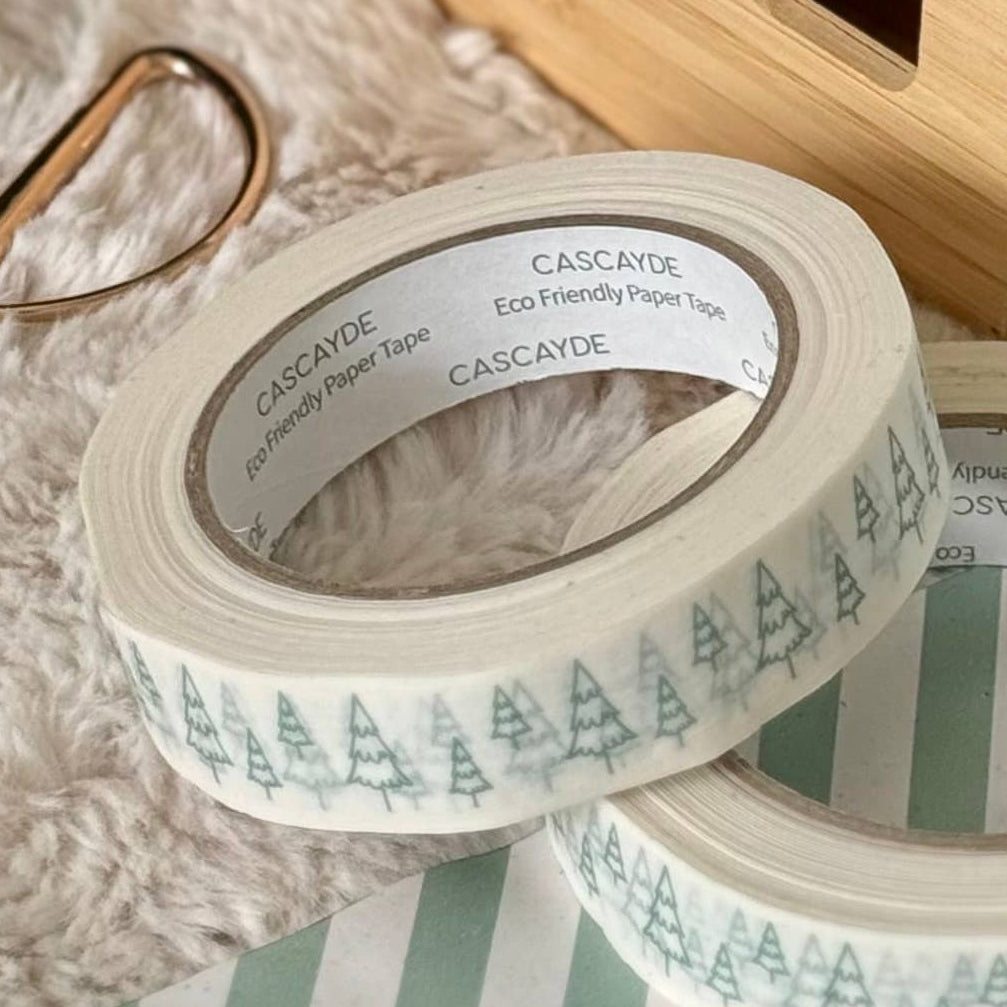 White paper packing tape with a pine tree pattern shown in a styled Christmas setting with wrapped presents, scissors, and a wooden tape dispenser.