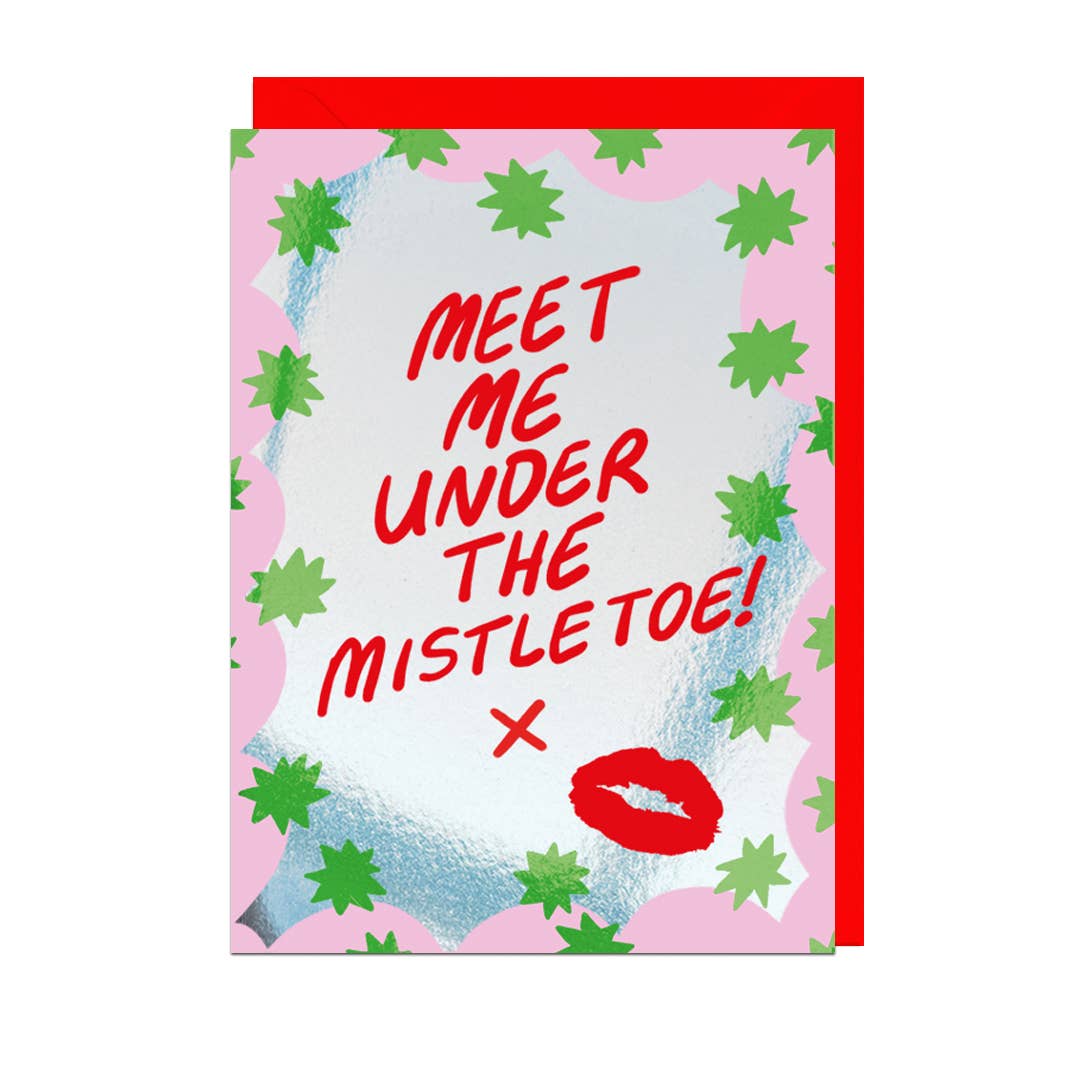 A festive greeting card with a red envelope, featuring the text 'MEET ME UNDER THE MISTLETOE!' in red script on a pink and silver background with green mistletoe illustrations and a red lipstick kiss mark.