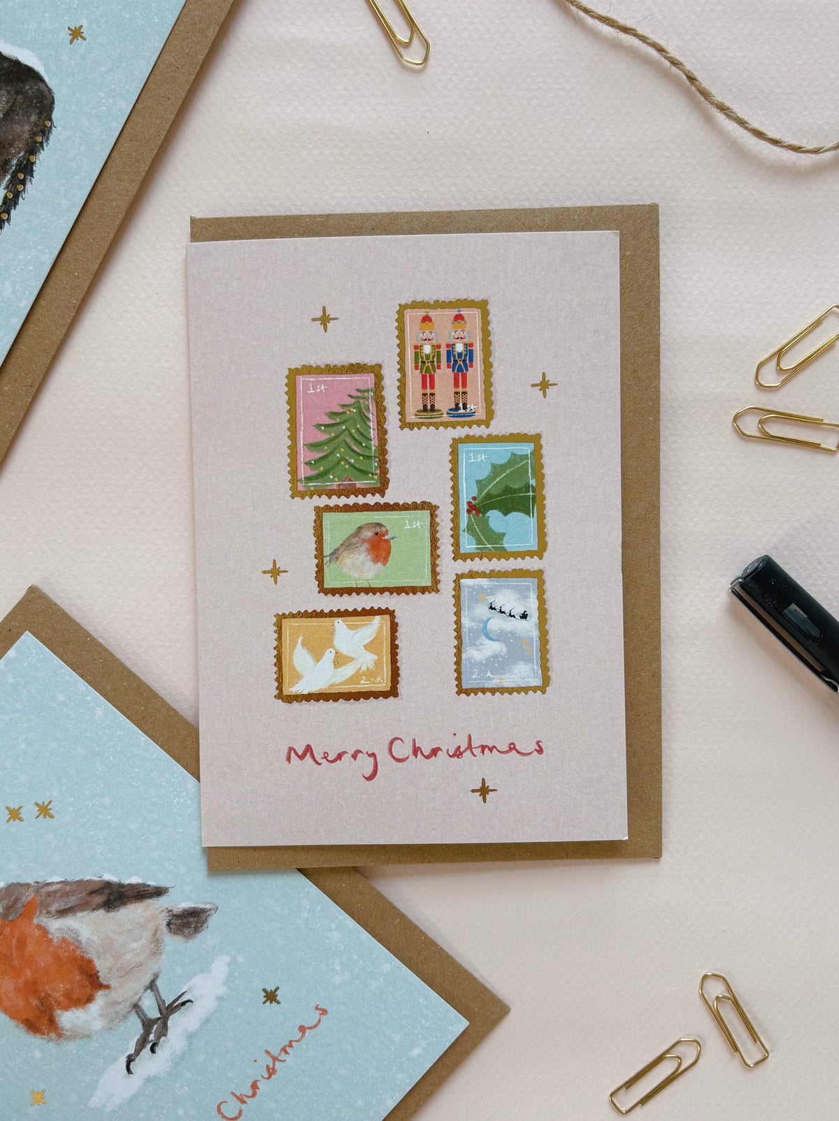 Festive Postage Stamps Christmas Card by lib's cards at penny black - shown on a table with stationery and other cards