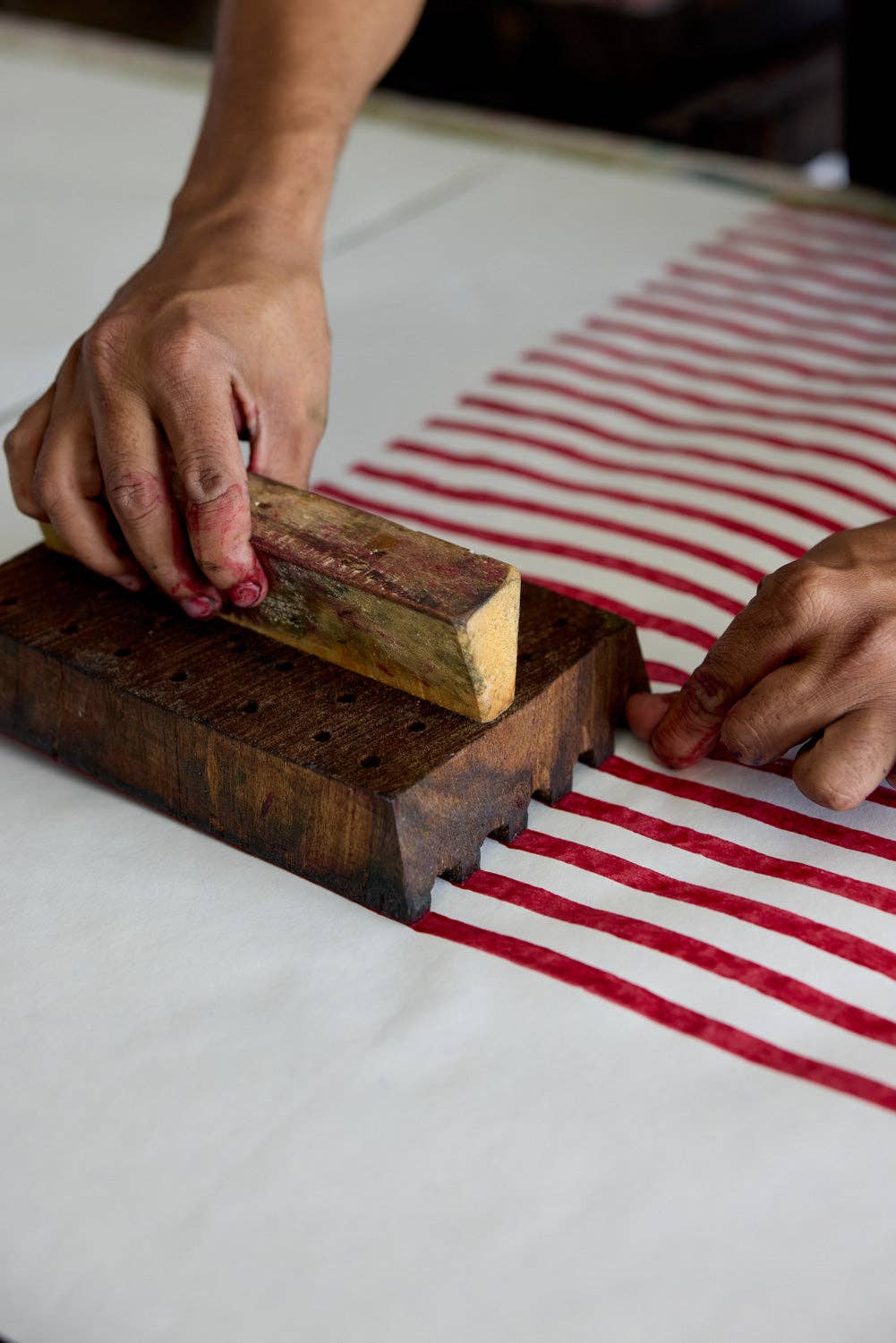 A person hand block printing red stripes onto white paper.
