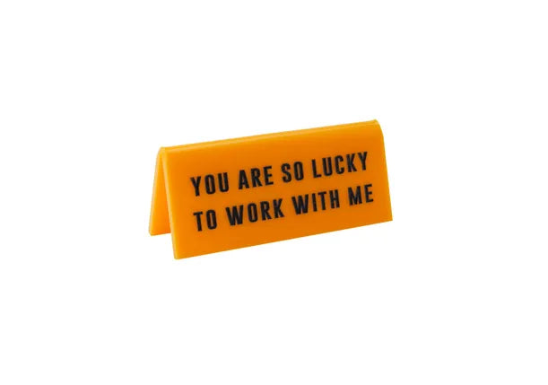 A small yellow acrylic sign that has in big black capital letters on it 'YOU ARE SO LUCKY TO WORK WITH ME'.