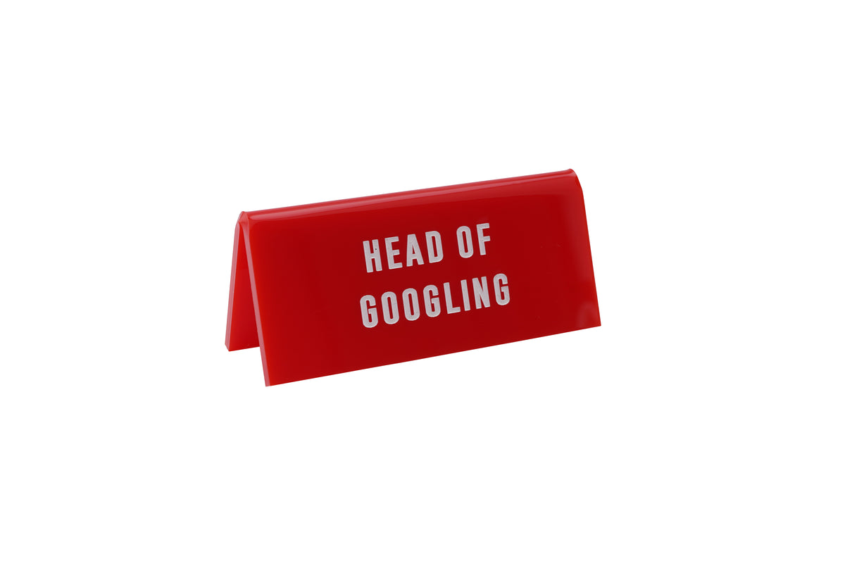 A small RED acrylic sign that has in big white capital letters on it 'HEAD OF GOOGLING'.