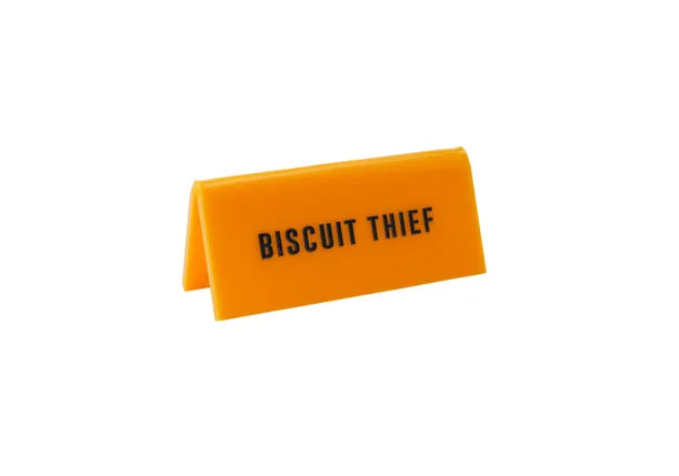 A small yellow acrylic sign that has in big black capital letters on it 'BISCUIT THIEF'.
