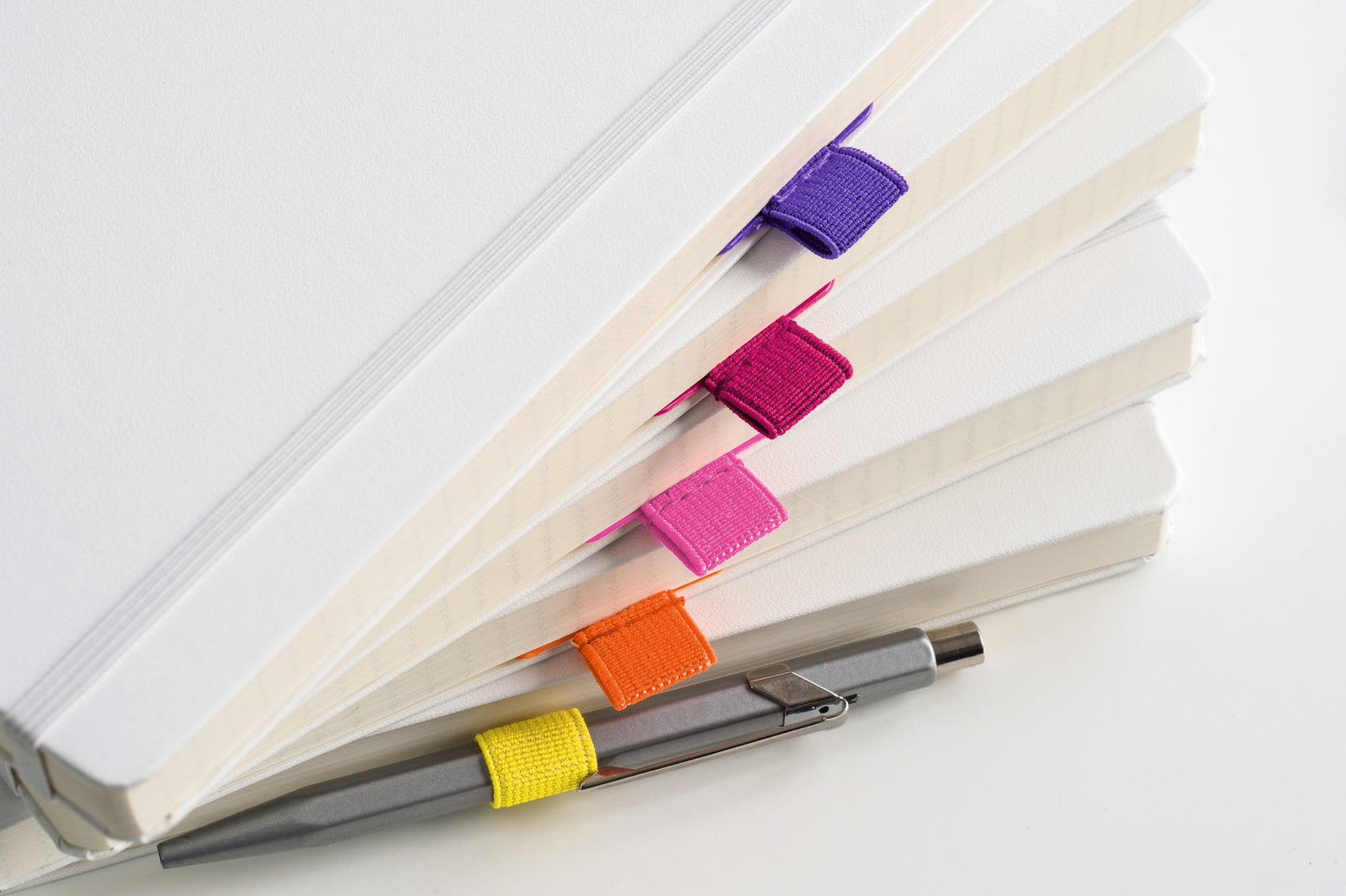 Leuchtturm1917 Pen Loop rainbow shown in white notebooks with a pen through the yellow one