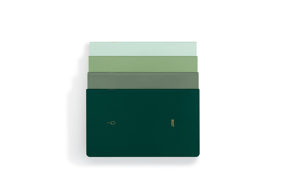 A stack of four slim rectangular notebooks in shades of green, with the top two in pale green and the bottom two in darker green, including a dark forest green cover with gold foil text and logo, set against a plain white background.