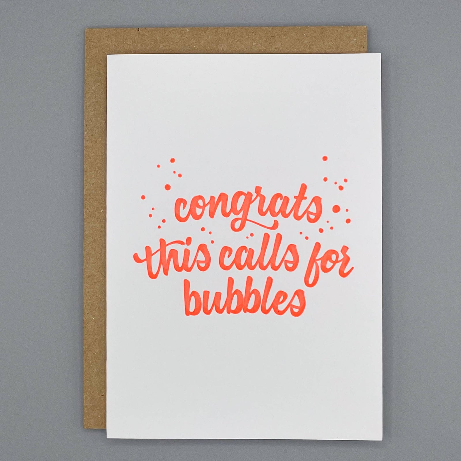 Letterpress congratulations card with orange text 'congrats this calls for bubbles' on a cream background