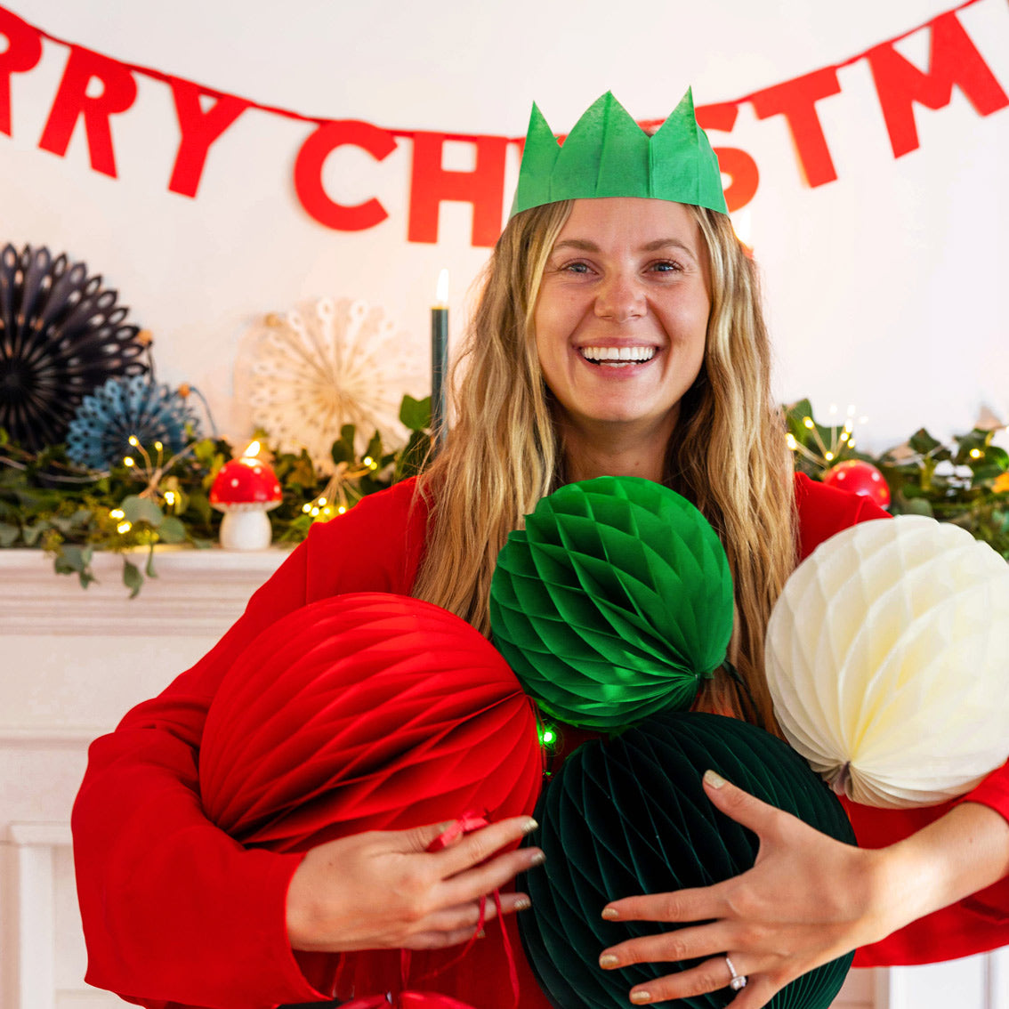An image of a person infront of a Christmas decorated fireplace, holding several honeycomb paper ball decorations.
