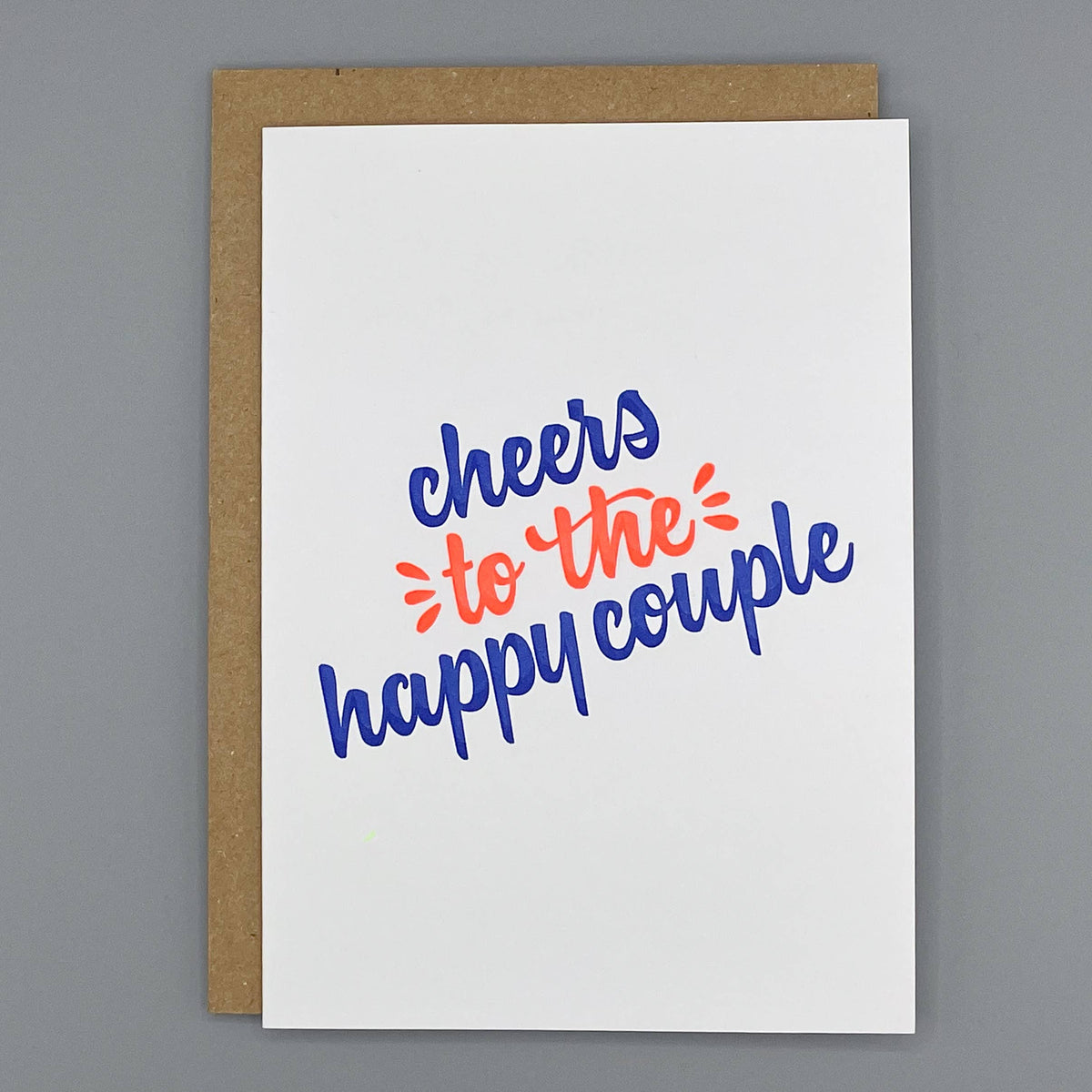 Letterpress congratulatory card with 'cheers to the happy couple' text on a cream background