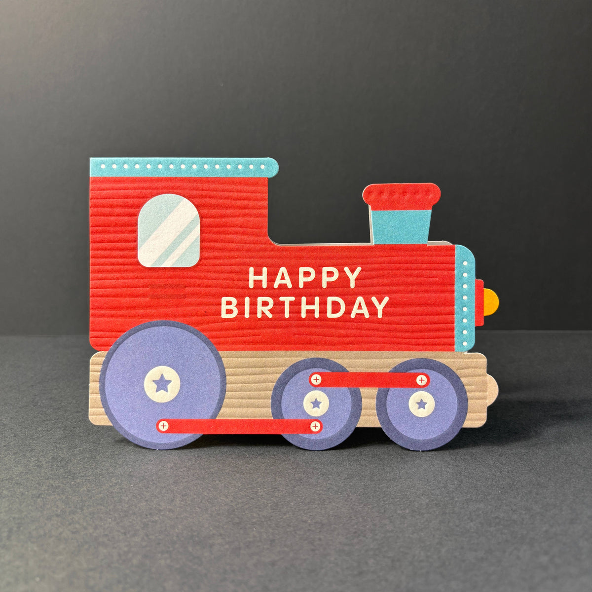 Red toy train cut out birthday card with 'Happy Birthday' text on a dark background by Heyyy cards at penny black