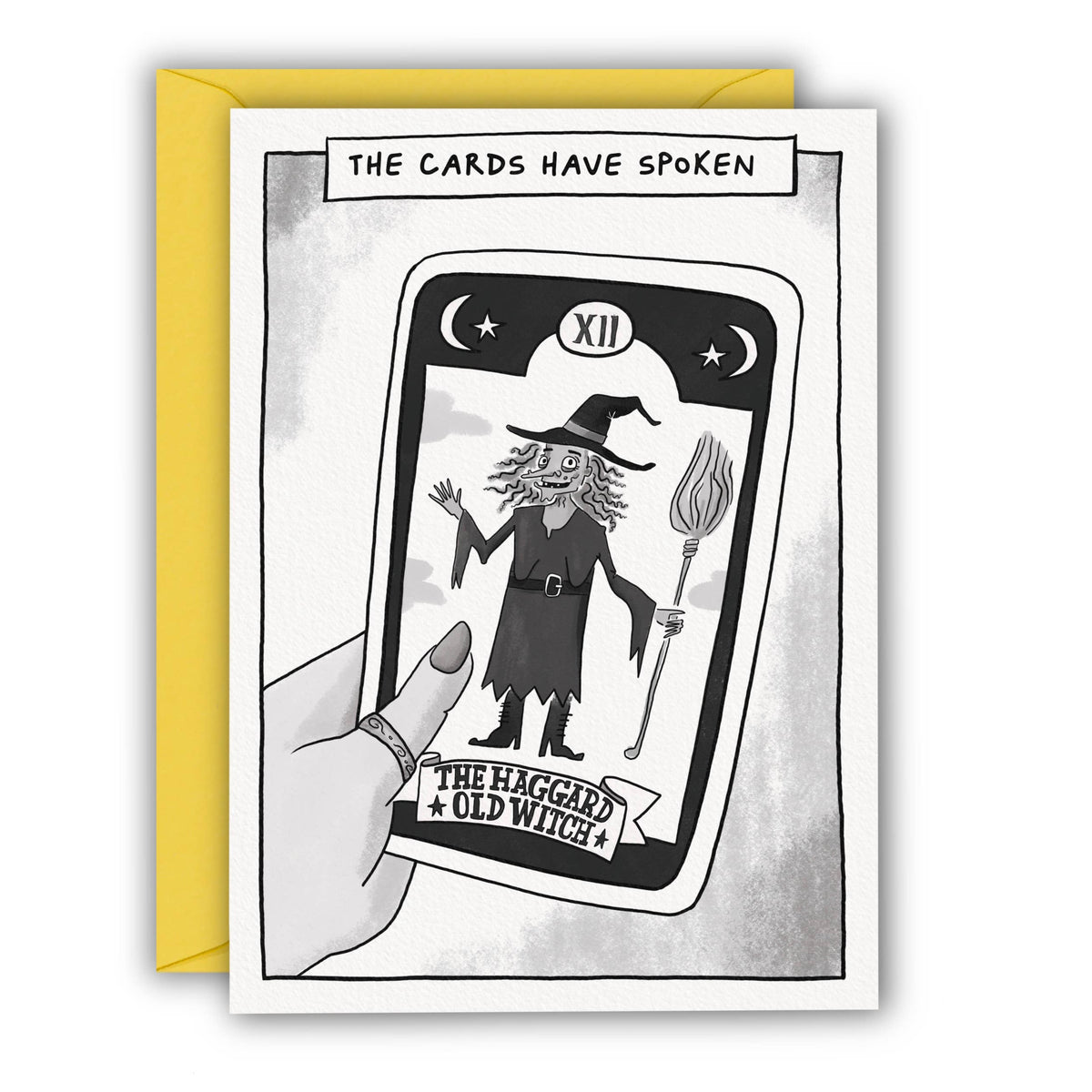 A greeting card with a black and white tarot card illustration reading 'THE CARDS HAVE SPOKEN' and 'THE HAGGARD OLD WITCH', shown with a yellow envelope behind it on a white background at penny black