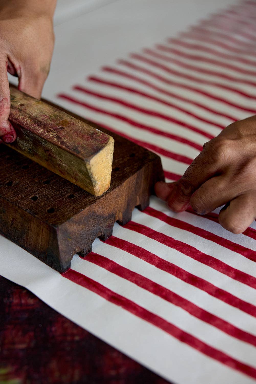 Person using a wooden tool to block print onto a red and white striped wrapping paper