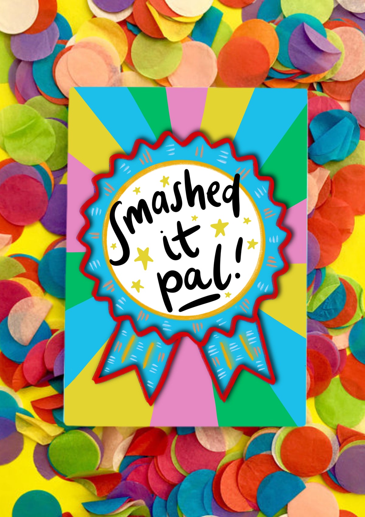 A greetings card with a rainbow sunbeam designed background with a large rosette motif. The rosette is light blue with red edging and has a large white circle in the middle that has the words handwritten 'smashed it pal'. The card is lying on a bed of rainbow confetti.