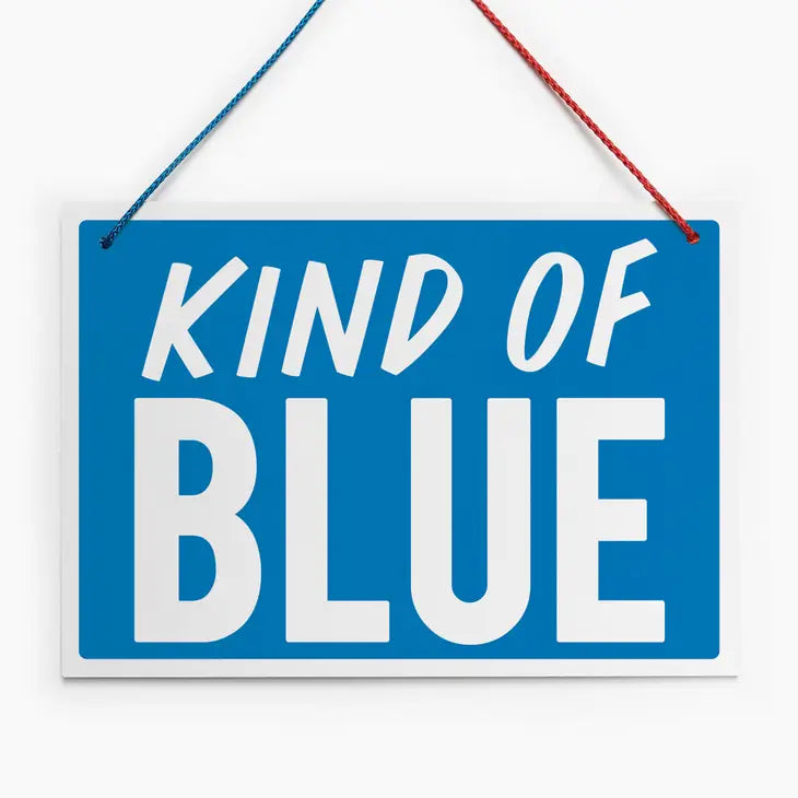An image of a blue hanging sign with a vintage feel. It has the words 'Kind of Blue' in white block capitals and a half red/half blue hanging cord.